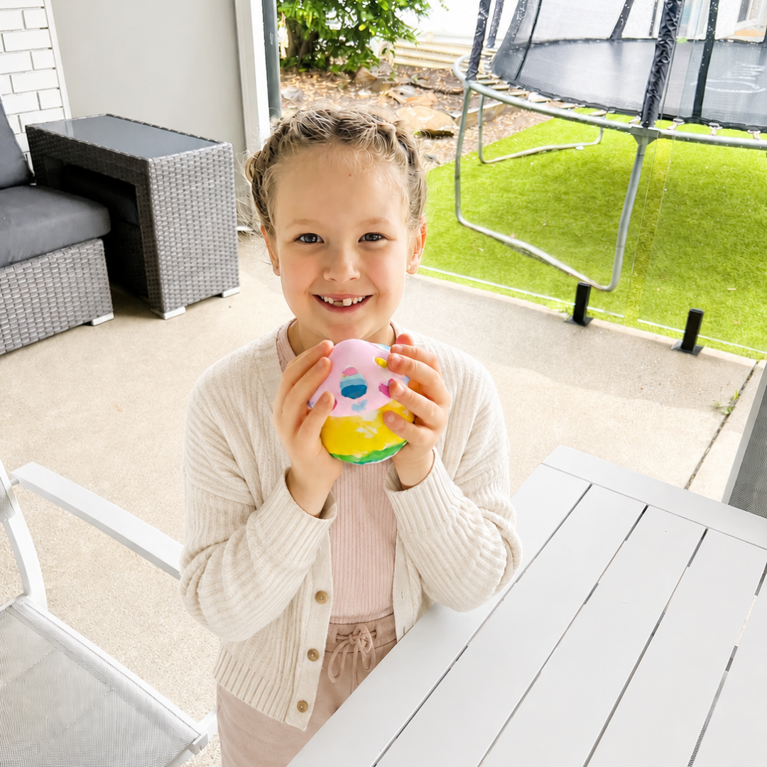 Young girl holding a mushroom potion pot in an outdoor setting with furniture and a trampoline.