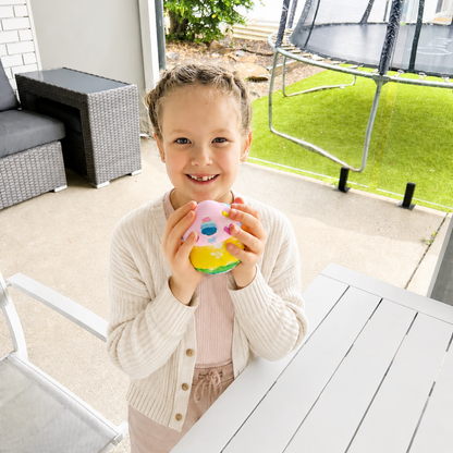 Young girl holding a mushroom potion pot in an outdoor setting with furniture and a trampoline.