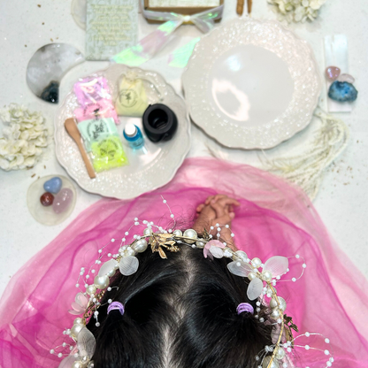 Person wearing a decorative headband with flowers and pearls, surrounded by decorative items on a white surface.